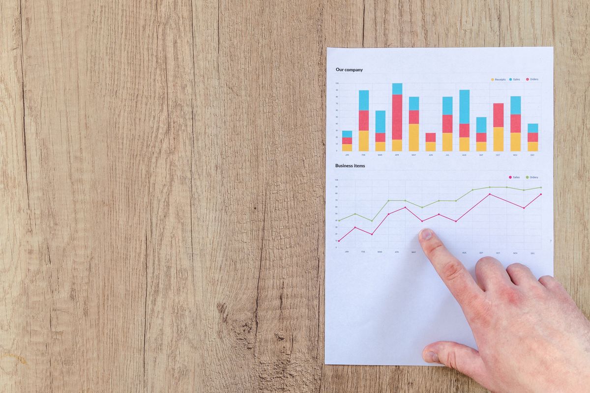 Hand analyzing business graphs on a wooden desk, focusing on data results and growth analysis.