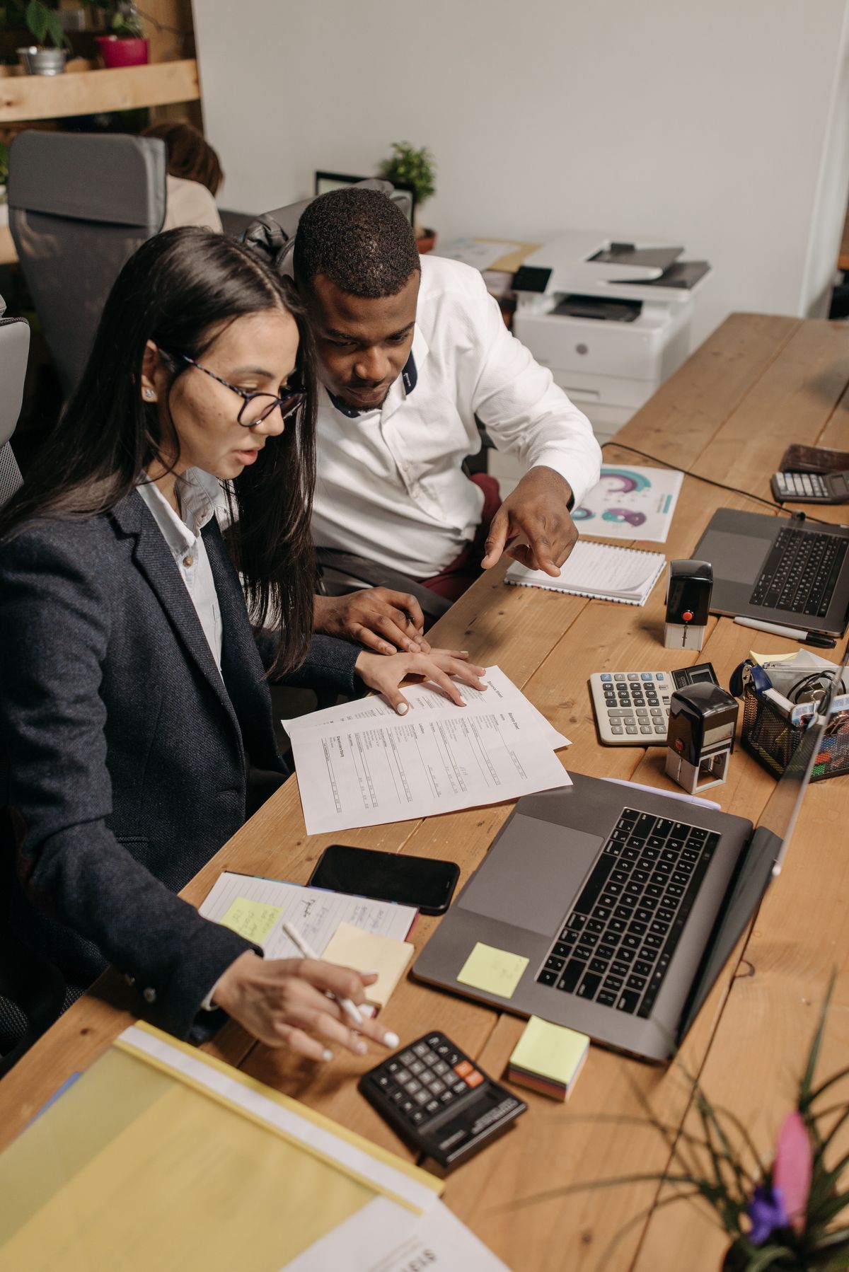 Colleagues working through paper records and a calculator at a shared desk