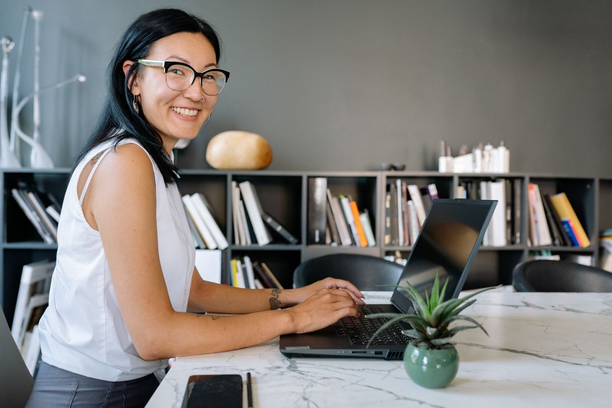 Cheerful businesswoman using a laptop at a desk in a stylish office with bookshelves.