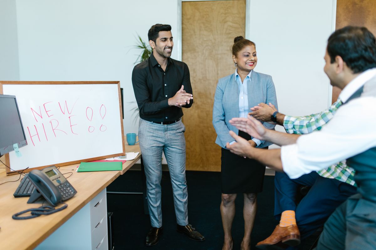 Colleagues welcoming a new hire in front of a "New Hire" whiteboard