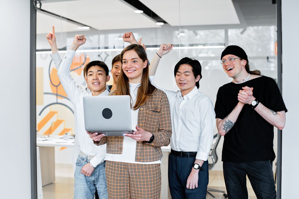 Group of diverse colleagues celebrating success while collaborating on a laptop indoors.