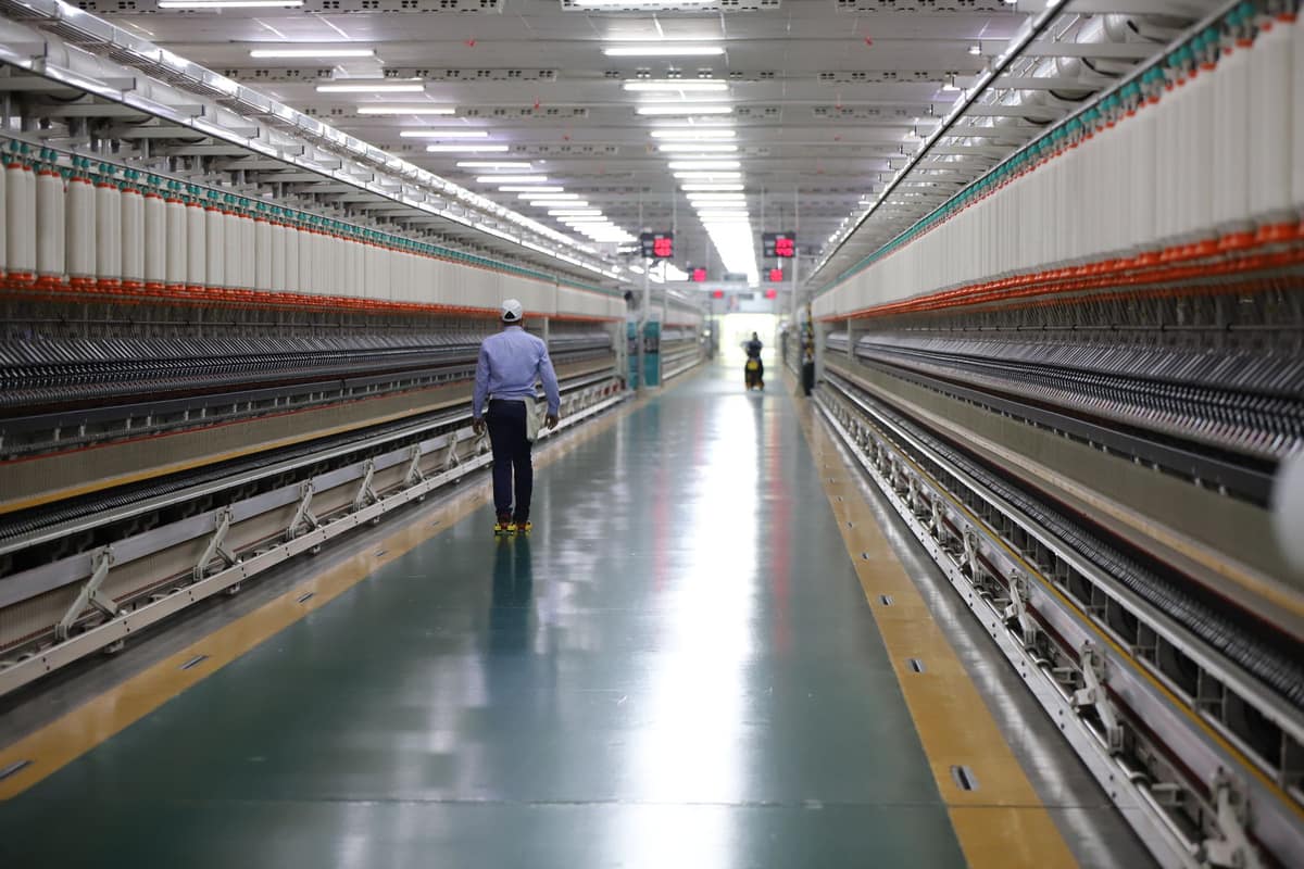 Long aisle of spinning machines in an Indian textile mill with a worker on shift