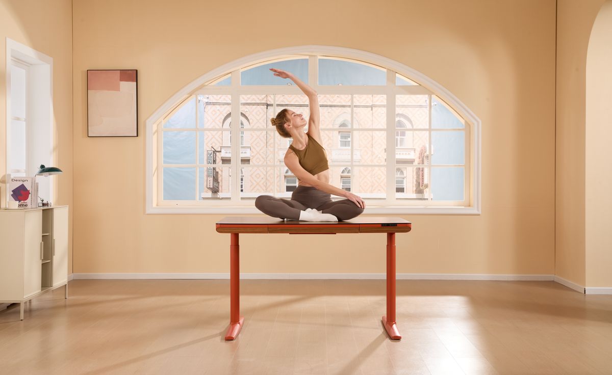 Woman doing a yoga pose on her desk in a bright office, representing work-life balance