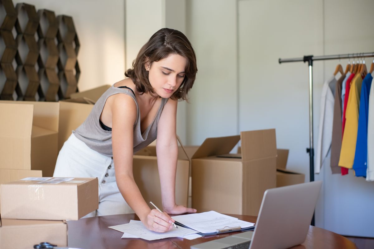 Young woman managing her small online business from a home office with boxes and a laptop.