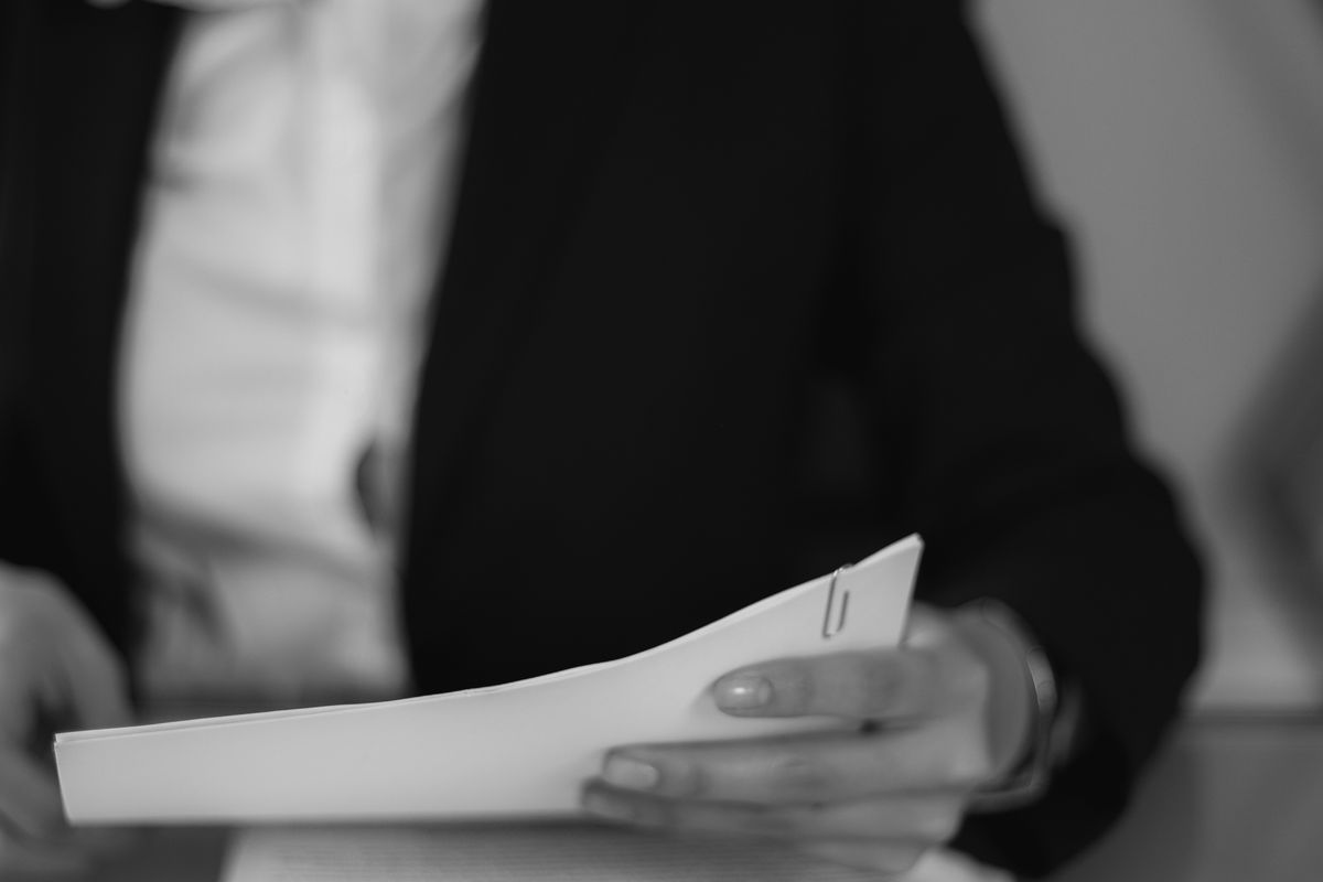 A businesswoman in formal attire reviews a stack of documents at her office desk.