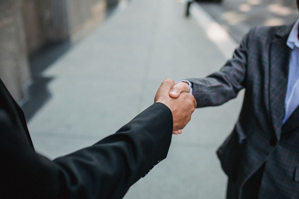 Close-up of two businessmen shaking hands outside, symbolizing partnership and agreement.