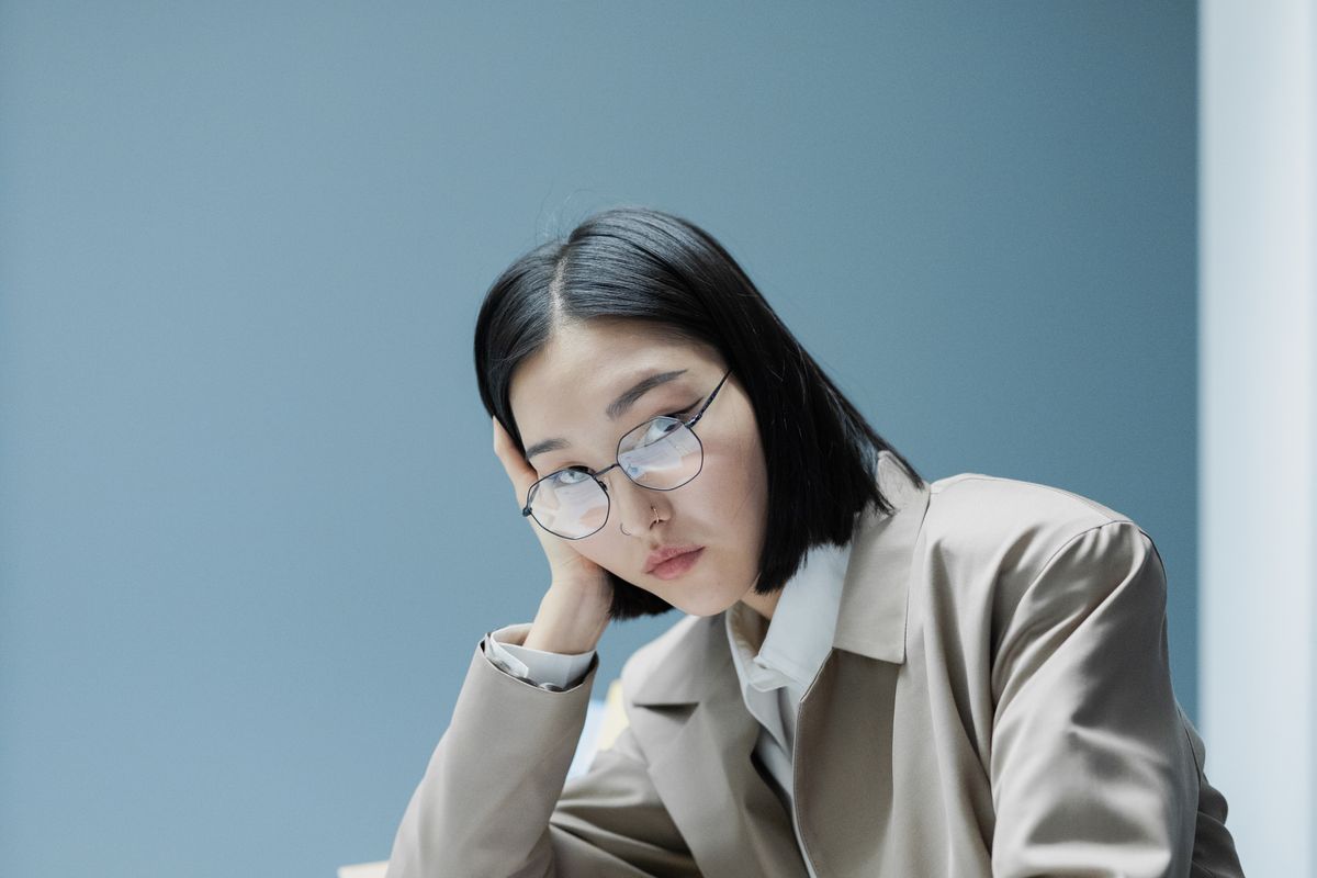 A woman in glasses appears bored while working at an office desk.