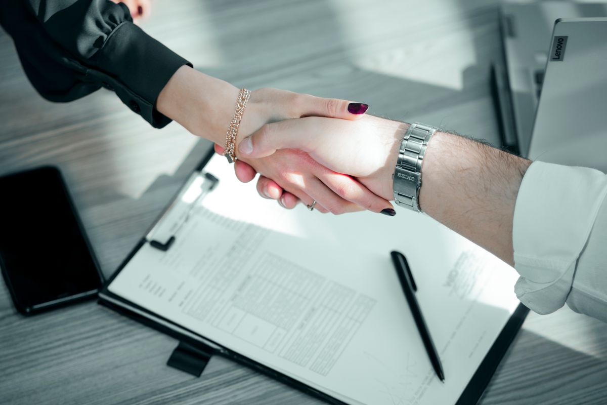 Handshake over a clipboard holding an invoice, closing a deal