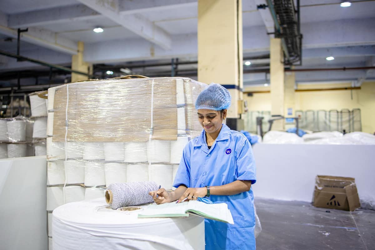 Worker in an Indian textile plant recording production details beside stacked rolls