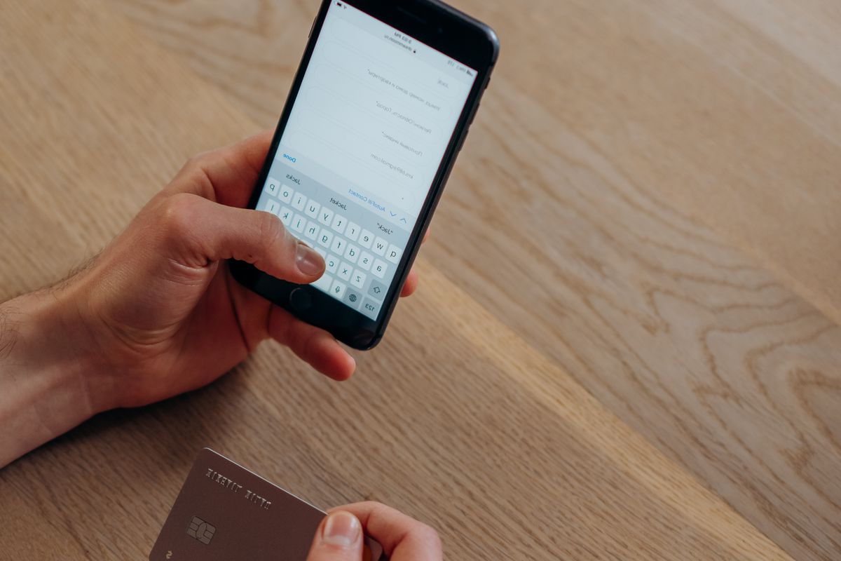 A person making a cashless transaction using a smartphone and credit card on a wooden table.