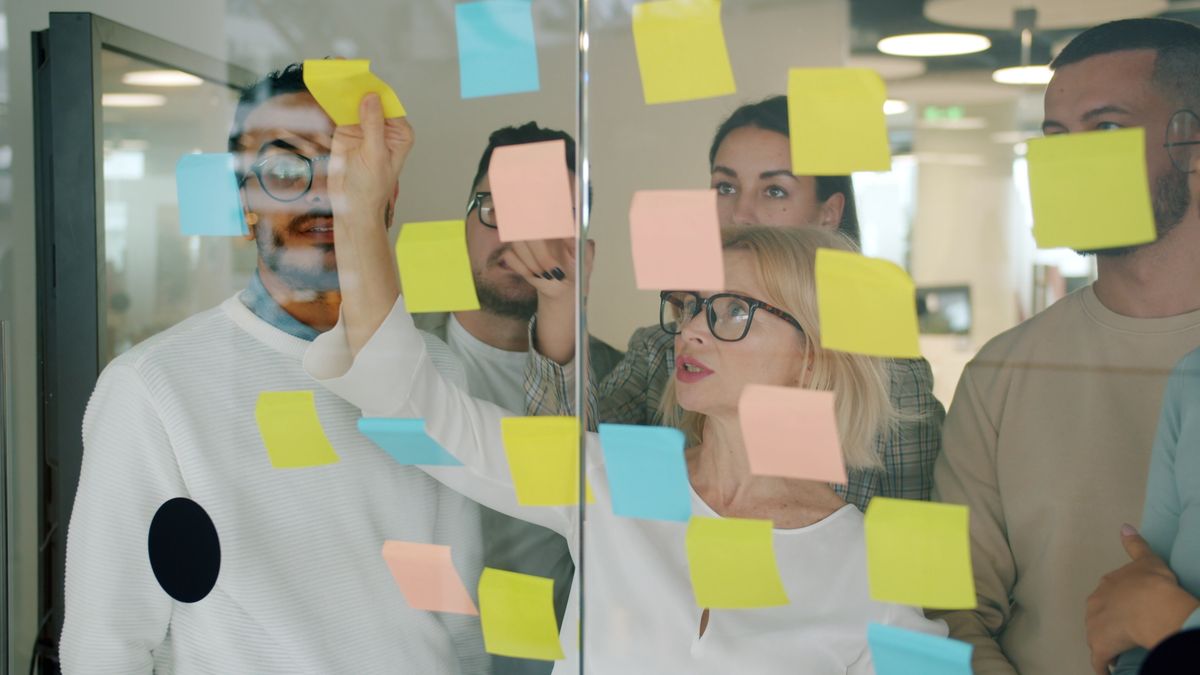 Team placing sticky notes on a glass wall to map a sales pipeline