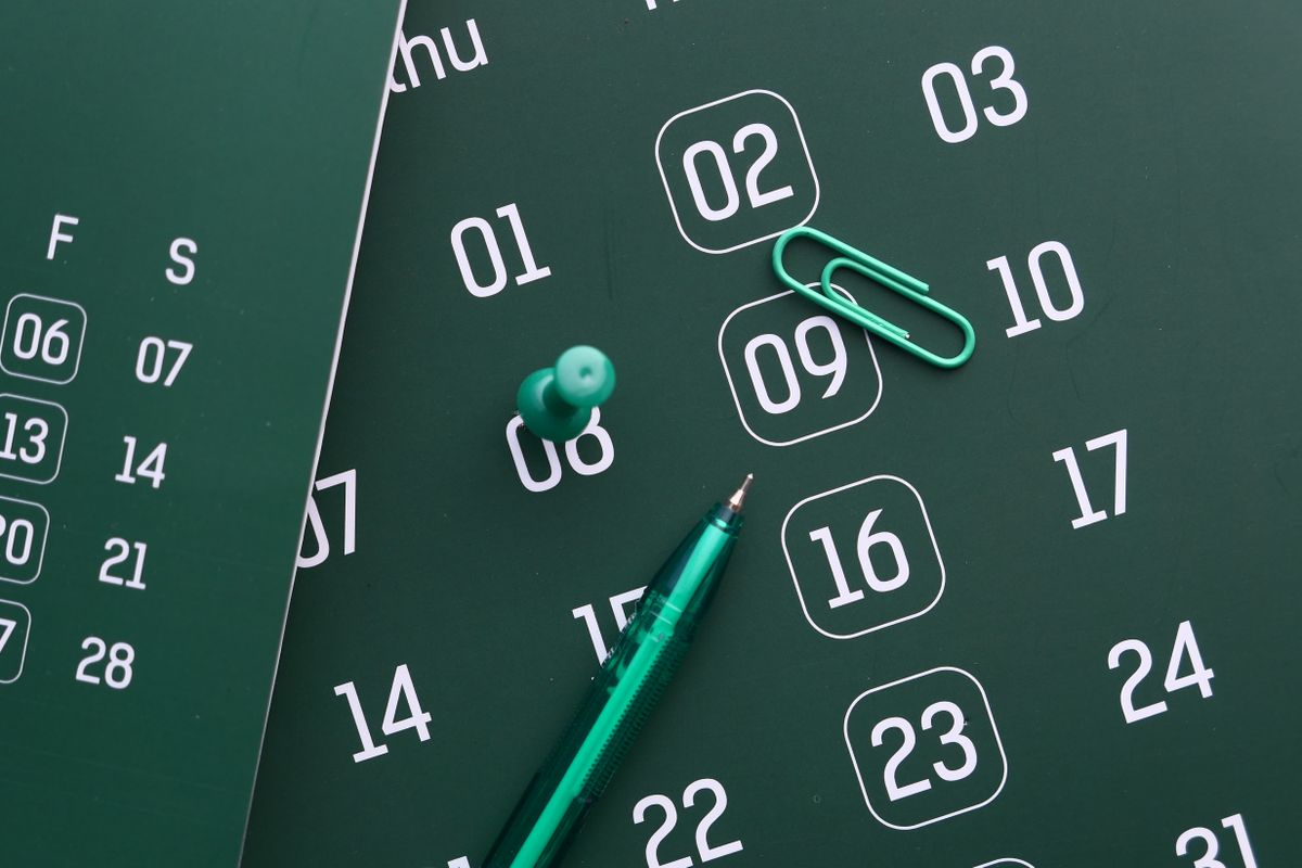 Green desk calendar with a pen, push pin and paper clip for planning days off