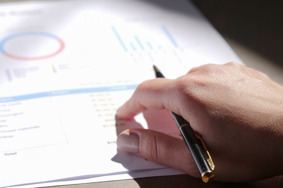 A close-up view of a hand holding a pen and examining financial charts on paper.