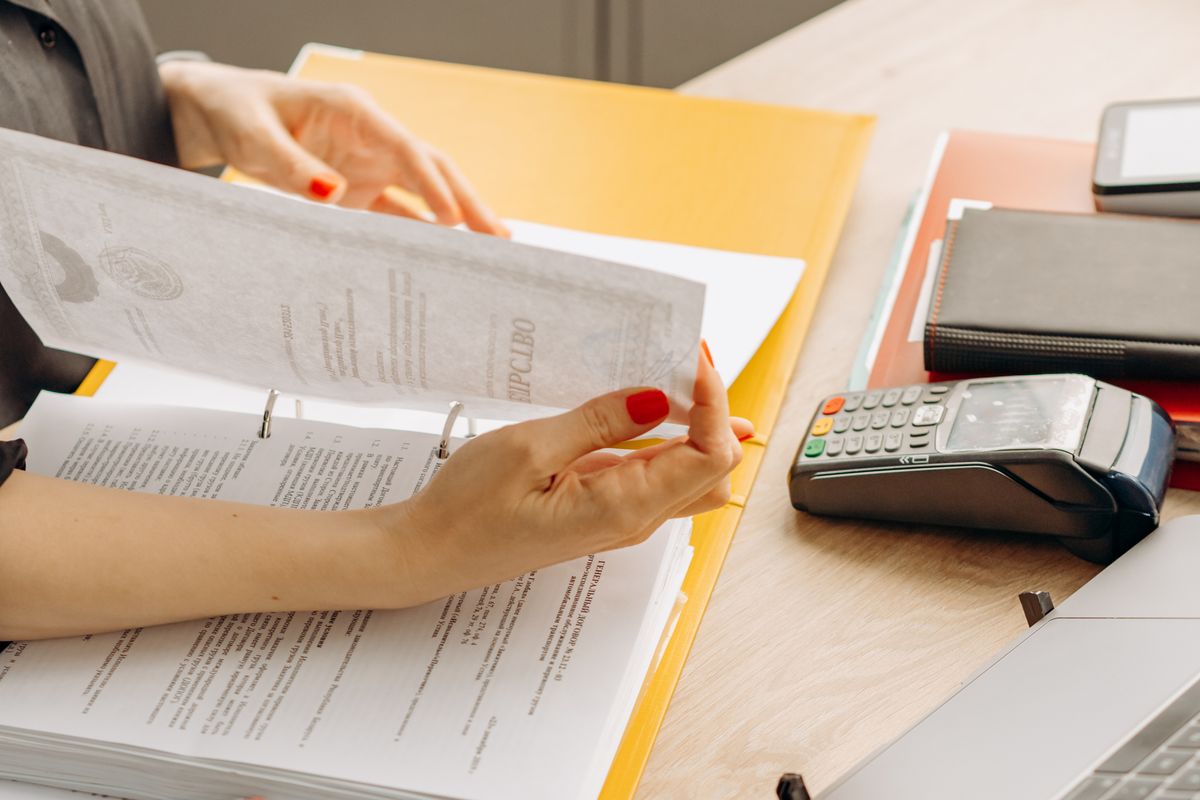 A woman flipping through financial documents on a wooden desk with various office supplies.