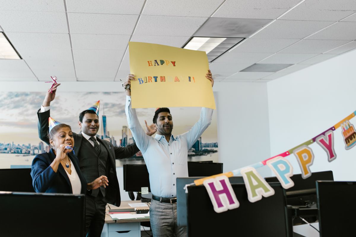 Colleagues cheering and holding a birthday banner to celebrate a coworker