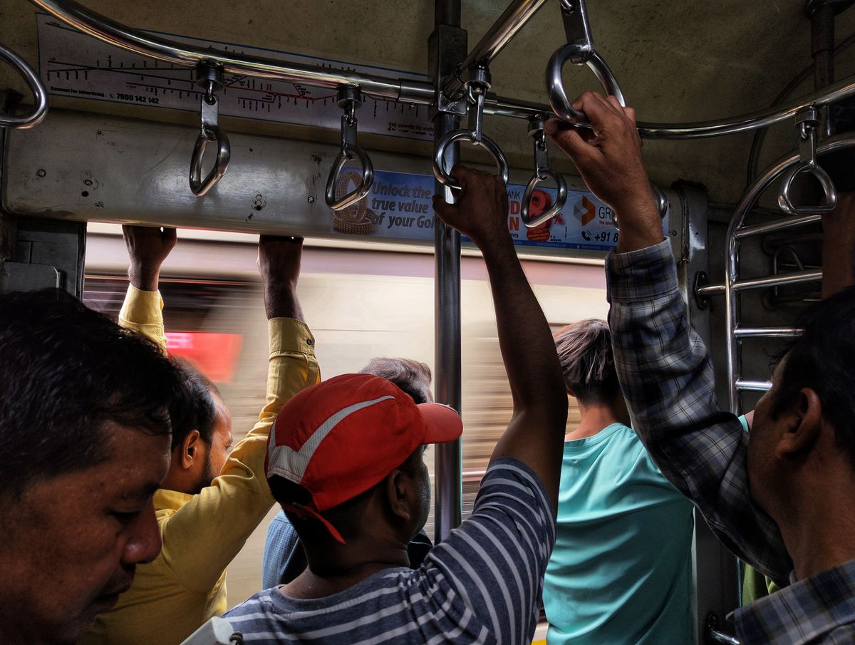Commuters holding handrails on a crowded Mumbai local train