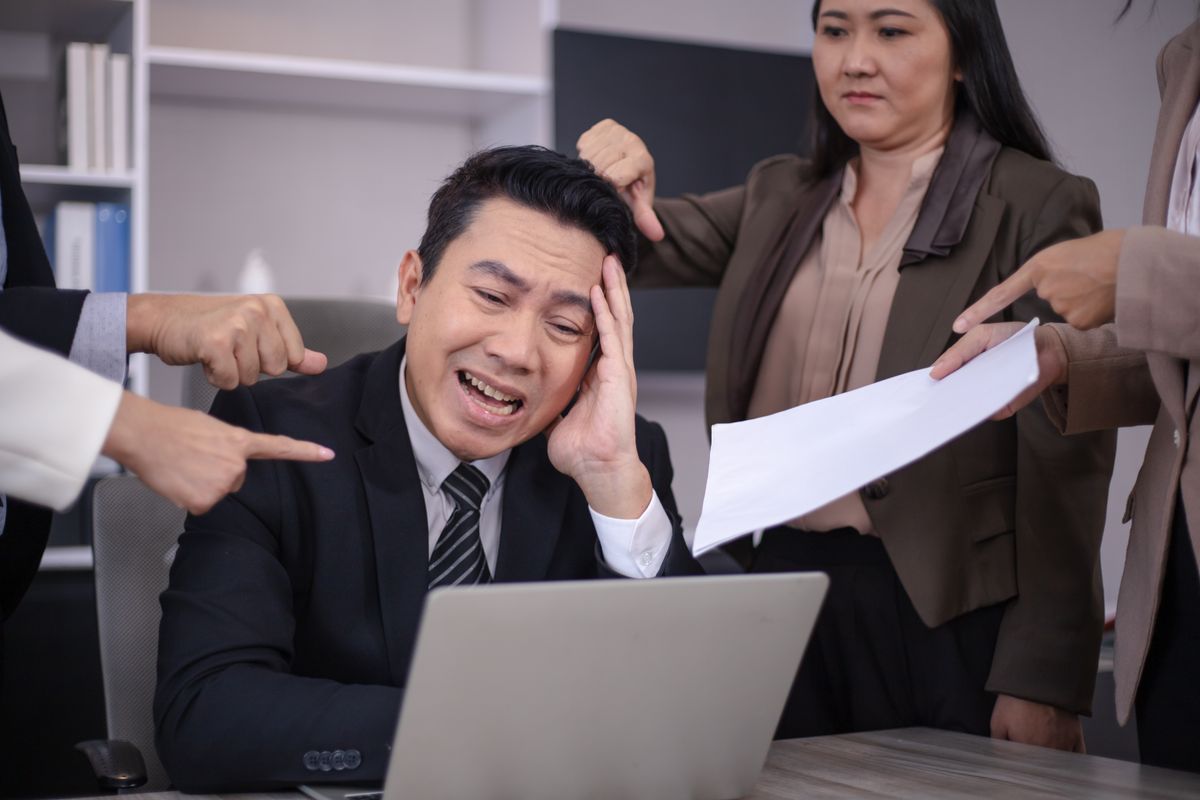 Stressed employee at a laptop while colleagues point fingers at him