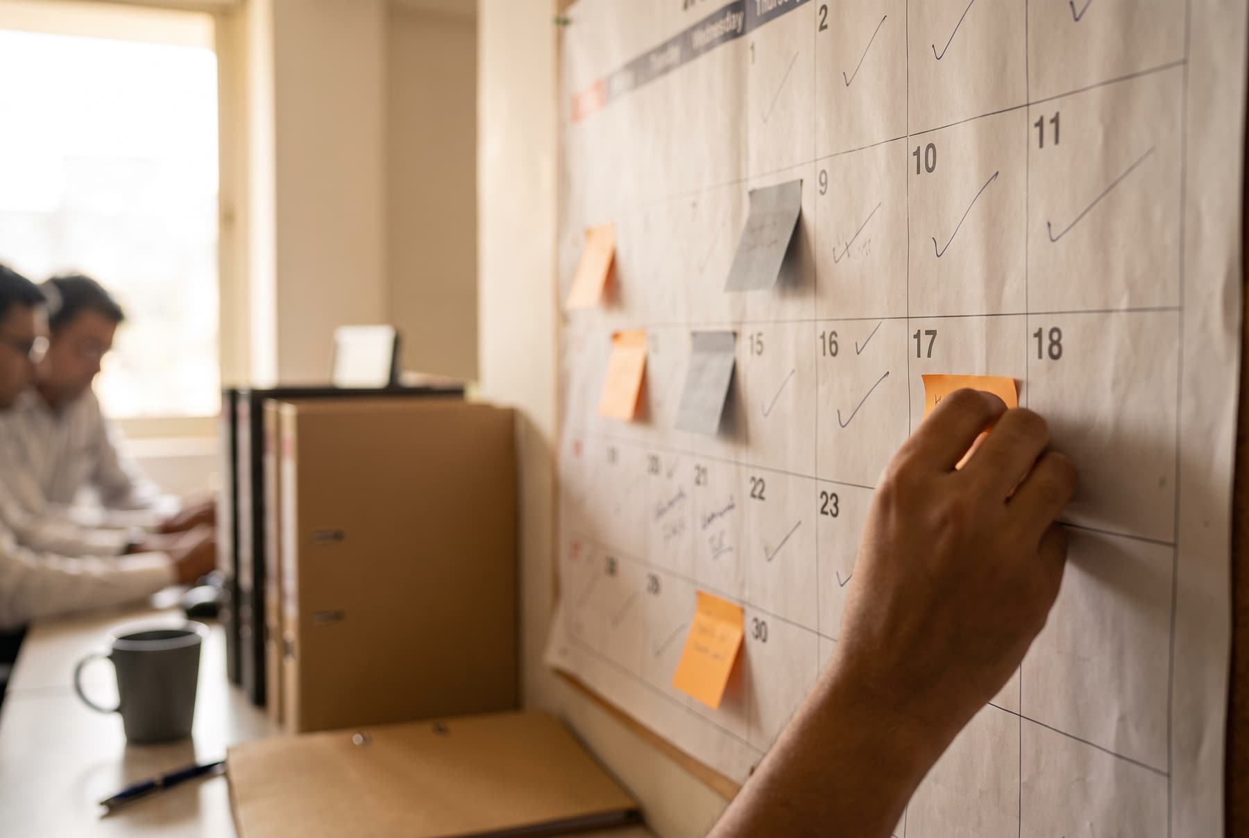 A hand pinning a note to a wall calendar marked with completed filings