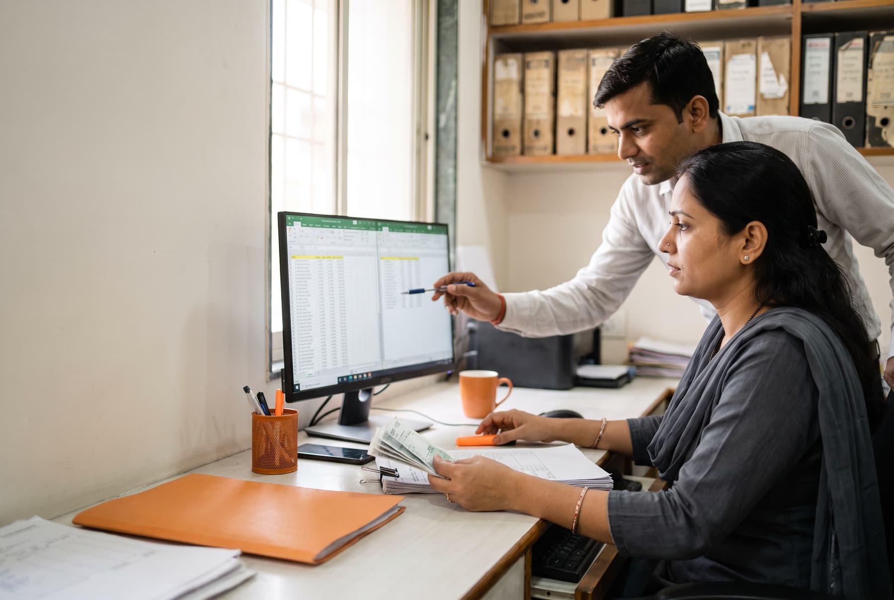 An accountant comparing the purchase register with GSTR-2B on a monitor while a colleague points at a row