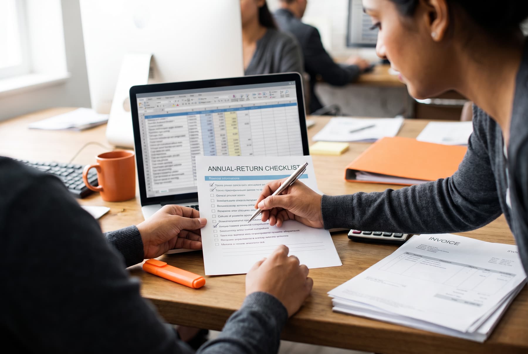 An accountant ticking an annual-return checklist next to a spreadsheet